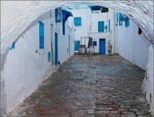 Дворик в  Сиди бу Али / &quot;Бело - голубой&quot; город в Тунисе . Характерен белыми стенами и синими дверями домов, узкими , извилистыми улочками, из которой вышла женщина в платке.