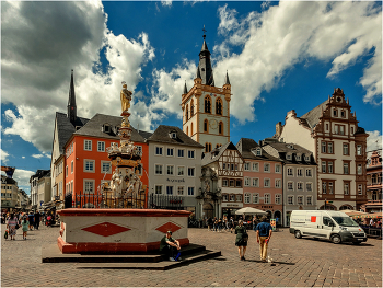 Рыночная площадь города Трир / По древней европейской традиции главной площадью в городе называют клочок земли, на котором и футбольное поле не уместилось бы. Трир не выделяется из общего ряда – Hauptmarkt (Рыночная площадь) представляет собой угол двух улиц с максимальным расстоянием между домами метров в 70.
Но согласно другой европейской традиции, даже на этих минимальных площадях горожане умудрялись разместить немало интересных достопримечательностей. В Трире это здания, выстроенные минимум в четырёх архитектурных стилях, а также Крест и Фонтан.