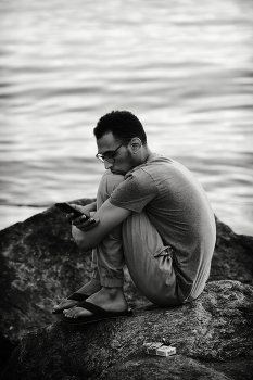 Он, море и телефон / Парень сидит на камнях на берегу моря, залипнув в телефоне