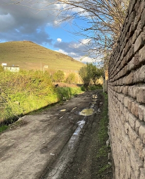 Peaceful Country Road / A peaceful rural road with green trees, a hill, and a beautiful cloudy sky.