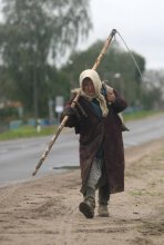 Сельский труд / Пожилая женщины несет косу по деревенской дороге.