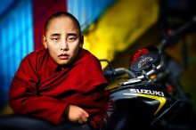 Biker Monk / Buddhist monk in red robe standing beside a motorcycle in a monastery in Kathmandu, Nepal.