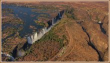 Водопад двух государств / Водопад Виктория находится на территории двух государств - Замбии и Зимбабве. Это самый большой водопад в мире протяжённостью около 1800 метров и высотой около 108 метров. Считается, что первым европейцем, увидевшим водопад, стал Дэвид Ливингстон. 17 ноября 1855 года, во время путешествия от верховьев Замбези к устью реки (1852—1856), Ливингстон достиг водопада и назвал его в честь королевы Виктории. Он написал о водопаде: Никто не может сравнить красоту с чем-либо увиденным в Англии. Это никогда прежде не видели глаза европейцев. На места, столь прекрасные, должно быть, смотрели ангелы в полёте. Самые древние известные науке жители области вокруг водопада были охотниками и собирателями, на их языках водопад назывался Shongwe, Amanza Thunqayo, Mosi-oa-Tunua («Гремящий дым»). Снимок сделан в сентябре 2012 года.