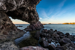 Береговая пещера на побережье в Сардинии / Вид на море, прибрежные камни, береговую пещеру и башню Нора рядом с Пулой. Сардиния, Италия.