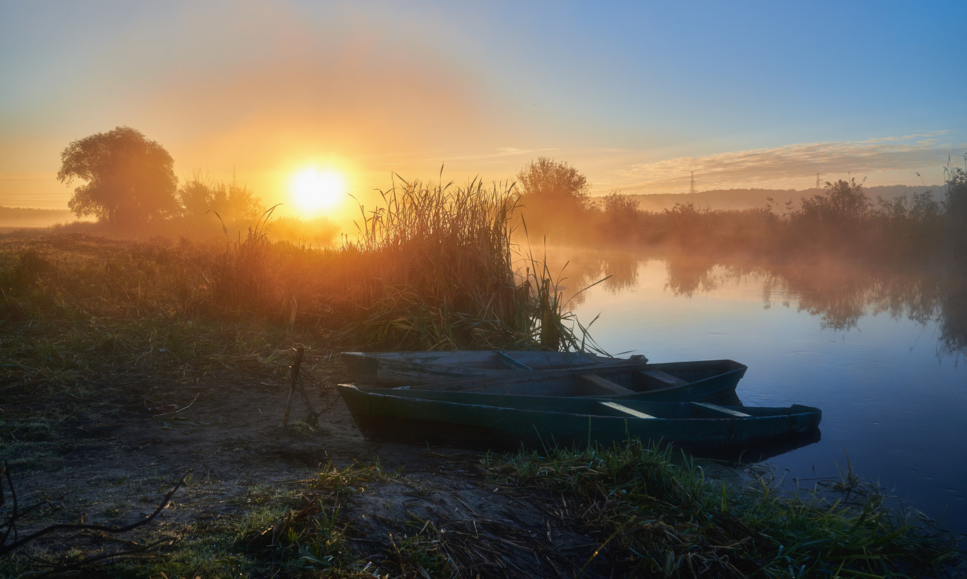 За деревней расстилается широкое поле. Утренний рассвет. Утро на реке. Одинокая лодка. Рассвет на реке лодка.